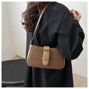 Détail du sac baguette en daim marron avec boucle en laiton sur un manteau noir