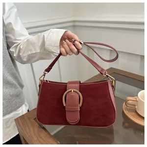 Détail du sac bandoulière bordeaux avec boucle fer à cheval dorée tenu par une femme