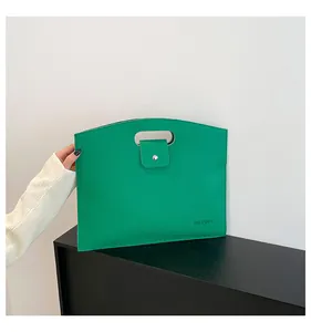 Detalle del bolso verde de cuero con grano de lichi, asa superior y botón de presión plateado