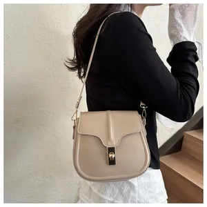 Beige saddle bag with golden twist lock and leather strap shown on a model