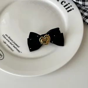 Detail eines schwarzen Samthaargummis mit goldenem Herzanhänger und silbernen Perlen