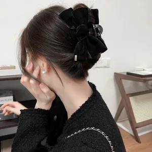 Dettaglio di una grande pinza per capelli con fiocco in velluto nero e targhetta dorata