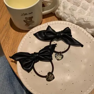 Detail of two black leather bow hair ties with gold heart pendants on a ceramic plate