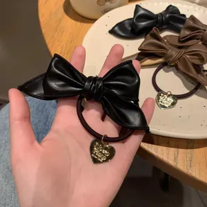 Detail of black and brown leather bow hair ties with a gold heart pendant on wood