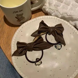 Detail of two coffee brown faux leather bow hair ties with gold heart charms in a cozy setting