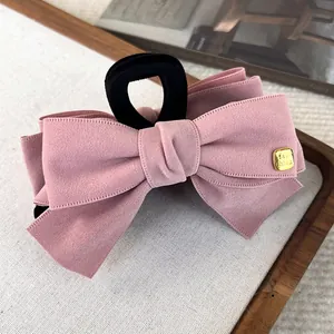Elegant dusty rose fabric bow hair claw clip with golden metal tag detail on a tray