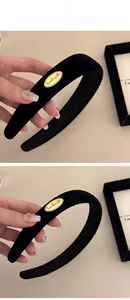 Détail d'un serre-tête en velours noir avec étiquette métallique dorée et texture douce