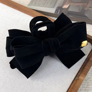 Detail of a black velvet bow hair clip with a luxury gold metal logo on fabric