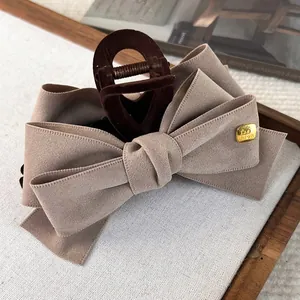 Detail of layered khaki fabric bow hair claw with gold fashion tag on wood tray