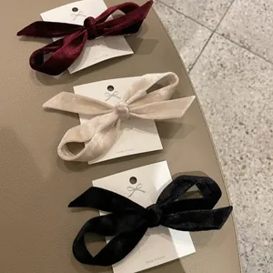 Three velvet bow hair clips in burgundy, cream, and black on a white display card