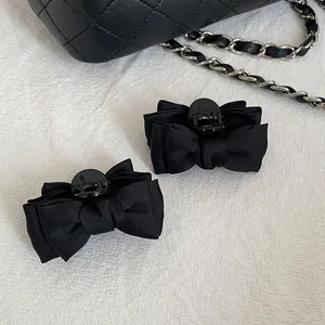 Detail view of two large black satin bow hair claws with elegant matte finish texture