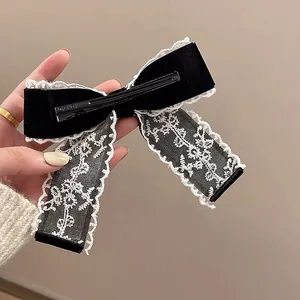 Lace bow hair clip with black satin and white embroidery in a handheld close-up view