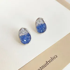 Close-up of irregular oval pearl earrings with silver edges and blue crystal inlay