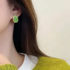 Elegant green crystal stud earrings with gold trim worn by a model in knitwear