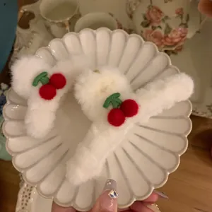 Detailaufnahme weißer Plüsch-Haarklammern mit roten Kirsch-Stickereien auf Keramik