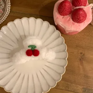Nahaufnahme einer weißen Plüsch-Haarklammer mit roten Kirsch-Stickereien auf Tablett