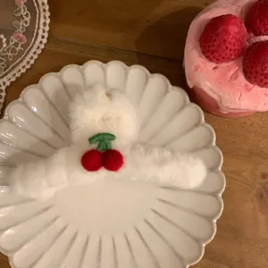 Detail einer Plüsch Haarklammer in Weiß mit Kirsch-Dekor auf einem Keramikteller