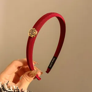 Détail d'un serre-tête en velours rouge avec rose dorée et étiquette fait main