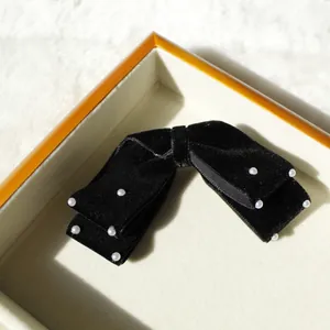 Eleganter schwarzer Samt-Bogen-Haarclip mit weißen Perlen auf einer Box