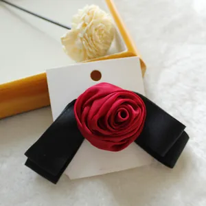 Elegante fermaglio per capelli con rosa di raso rosso e fiocco nero su cartoncino