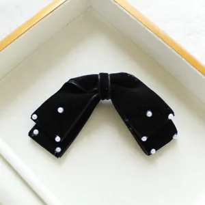 Eleganter schwarzer Samt-Haarclip mit weißen Perlen auf einem dekorativen Holztablett