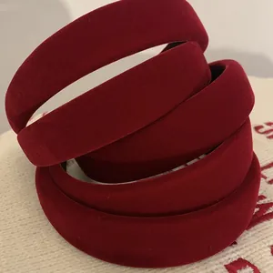 Close-up of stacked burgundy velvet padded headbands on a cream knit background