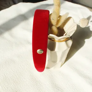 Eleganter Haarreif aus rotem Samt mit gravierter Goldplakette auf schlichtem Hintergrund