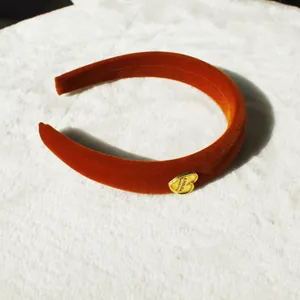 Thick velvet headband in pumpkin orange with golden heart detail on soft white carpet