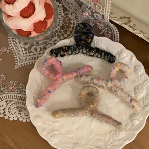 Detail of four colorful knit hair claws on a ceramic plate with lace and dessert