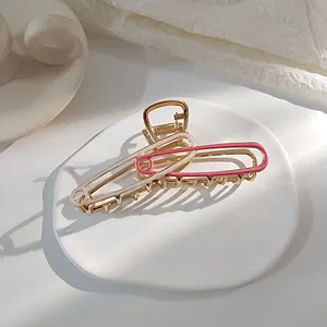 Detail van grote paperclipvormige gouden haarklem met roze emaille op een wit dienblad