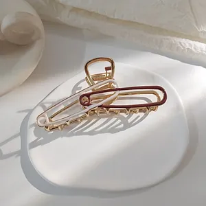 Detail van een grote gouden metalen haarklem met rood en wit emaille accenten