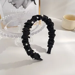 Détail d'un serre-tête en tissu plissé noir avec perles blanches sur support verre