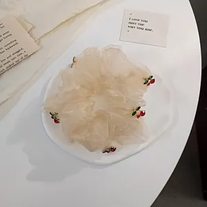Detail of cream organza scrunchie featuring cute red cherry charms on white tray