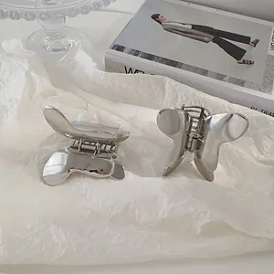 Close-up of dual silver butterfly hair claws made of polished metal on white artistic paper