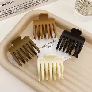 Detail of four matte hair claw clips in neutral colors on a minimalist beige tray