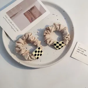 Close-up of beige satin scrunchies with checkered heart and rhombus charms in a ceramic plate