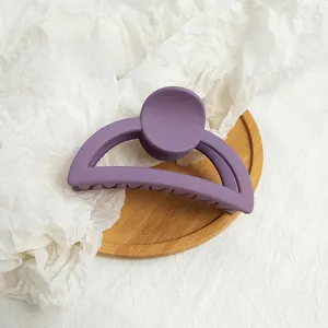 Macro detail of purple matte hair claw clip on a rustic wooden tray and white textured fabric