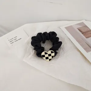 Detail of satin scrunchie featuring a black and white checkerboard heart metal charm
