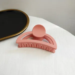 Close-up of a matte pink semicircular hair claw clip on a textured surface