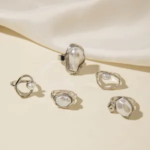Makroaufnahme von 5 silbernen Ringen mit Barockperlen auf weißem Seidenstoff für Damen