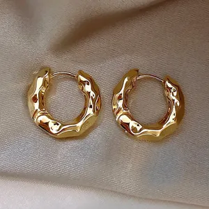 Gros plan de boucles d'oreilles créoles dorées texture lave sur tissu en soie champagne