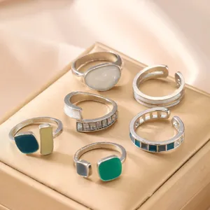 Detailed close-up of six geometric enamel rings on gold jewelry box with satin background