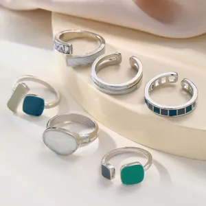 Macro shot of silver geometric enamel rings with colorful zircon inlays on soft silk background