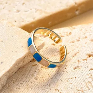 Close-up of gold-plated open ring featuring geometric blue and pink enamel blocks