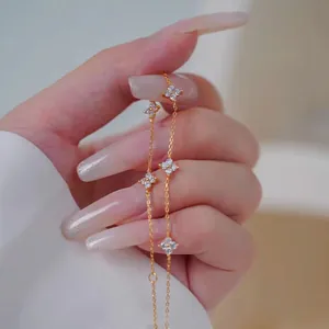 Macro view of gold clover necklace with zircon pave charms held by a hand
