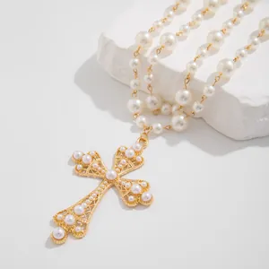 Detailed close-up of a golden hollow cross pendant with pearls on a textured stone surface