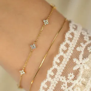 Close-up of golden four-leaf flower bracelet with zircons on a white lace sleeve background