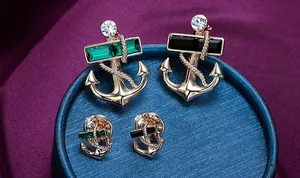 Macro shot of rose gold nautical anchor brooches with emerald crystals and silk background