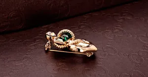 Detailed close-up of emerald-cut green crystal brooch with golden twisted metal frame