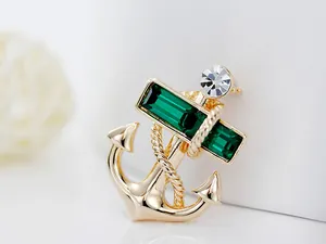 Macro shot of gold-plated anchor brooch featuring green crystals and white rhinestones